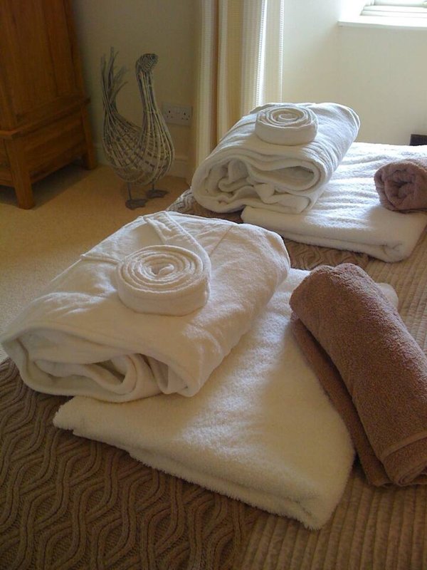 Bedroom with rolled towels and linens arranged on bed, wooden door and decorative vase visible
