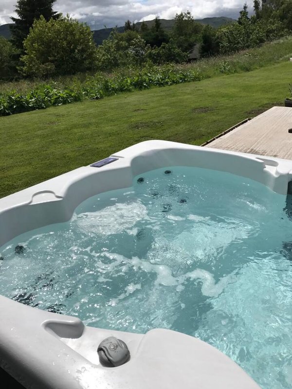 Hot tub with jets running, wooden deck, manicured lawn and mountain views