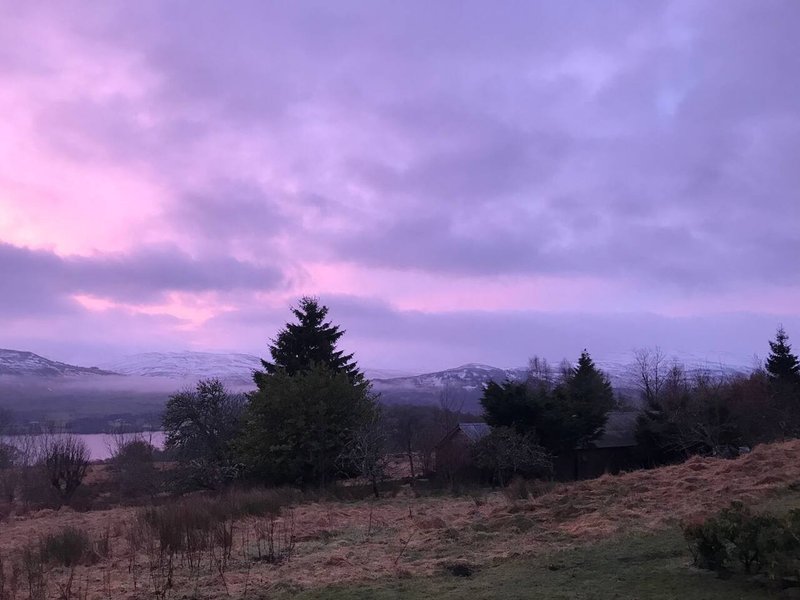Twilight landscape view with evergreen trees, distant mountains and lake under purple sky