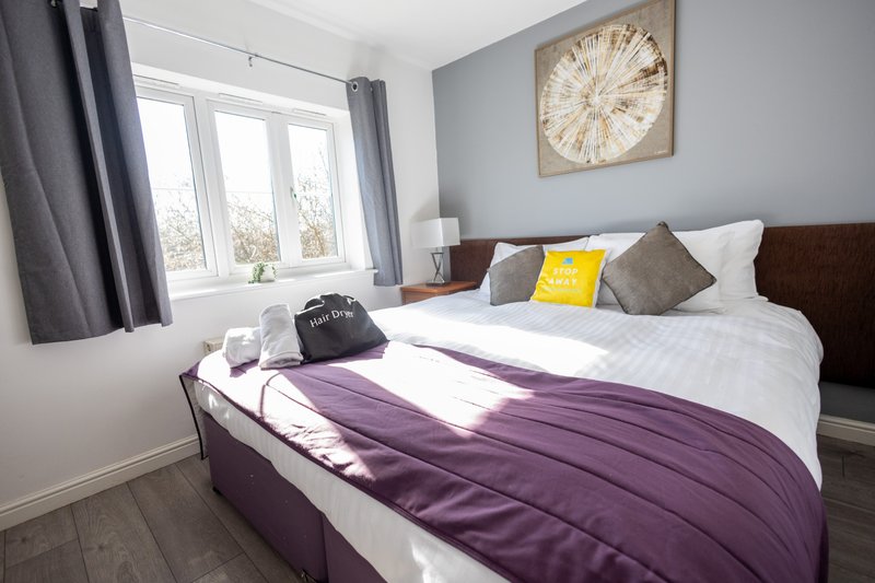 Bedroom with double bed, purple bedding, decorative pillows, wooden headboard, and wall clock