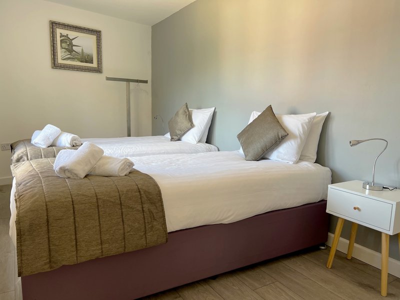Bedroom with double bed, white pillows, gold throw, wooden nightstand and floor lamp