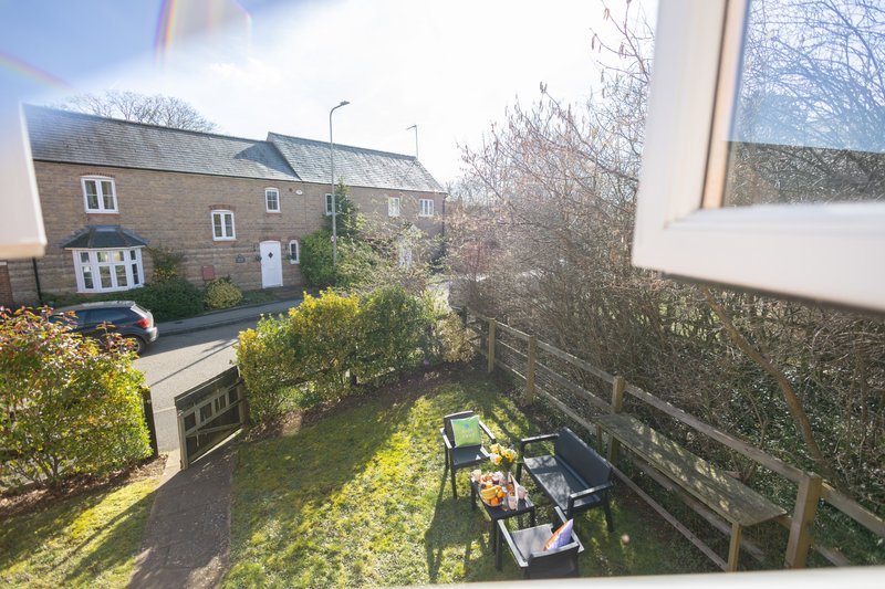 Garden view with patio furniture, hedges, and stone cottage exterior beyond fence