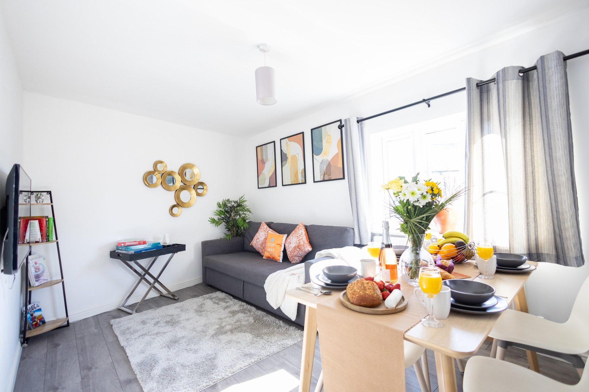 Modern living room with gray sofa, dining table, wall art, and bright window with curtains