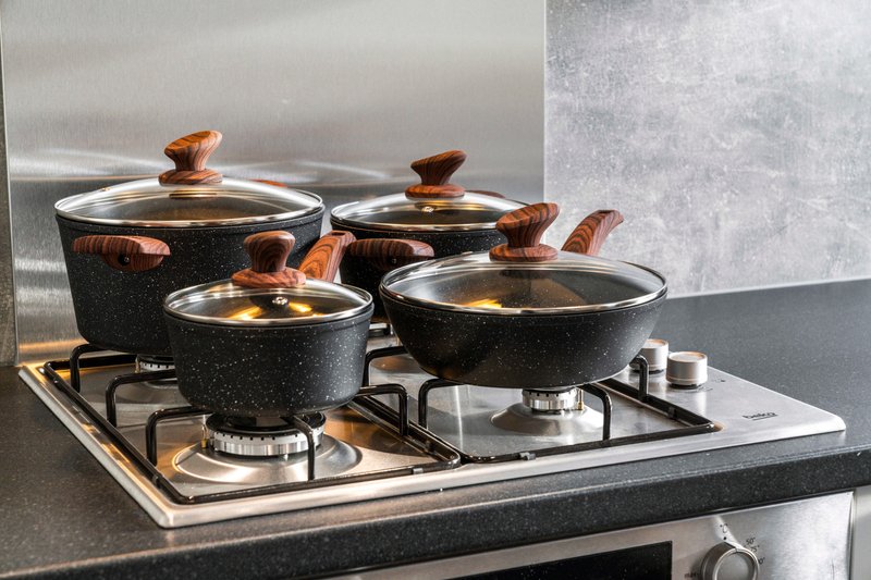 Kitchen stovetop with four black speckled cookpots with wooden handles on gas burners