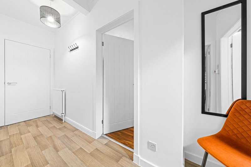 Modern hallway with wooden flooring, white walls, mirror, and orange chair