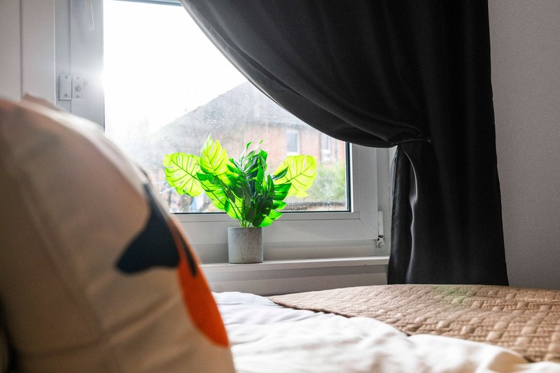 Bedroom with double bed, window with black curtains, potted plant on sill
