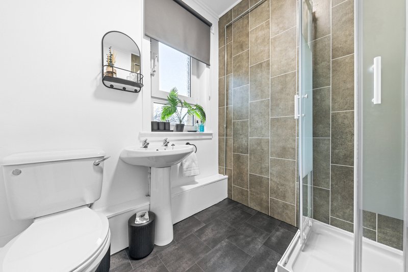 Modern bathroom with toilet, pedestal sink, shower enclosure and tiled walls