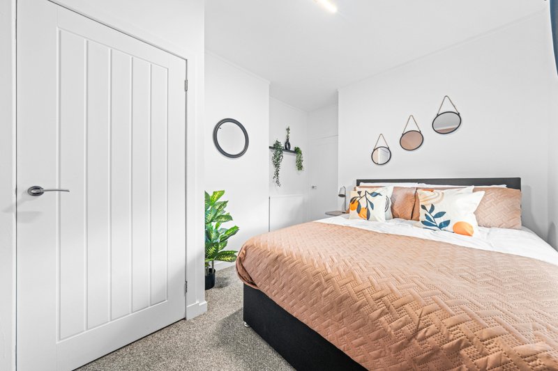 Modern bedroom with double bed, peach bedding, white wardrobe and decorative hanging mirrors
