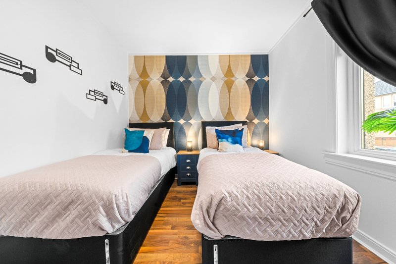 Modern bedroom with two single beds, geometric headboard, wooden floor and natural light