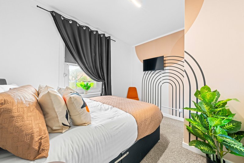 Modern bedroom with double bed, cushions, dark curtains, potted plant and minimalist wall art