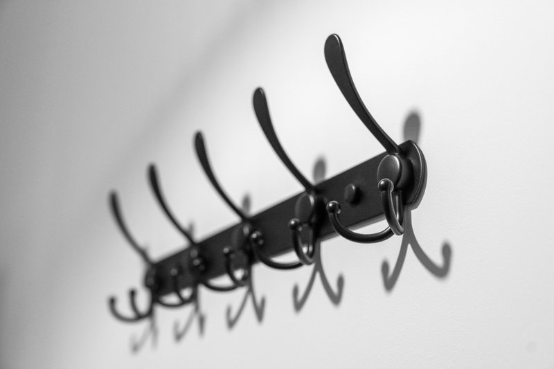 Black wall-mounted coat rack with multiple hooks against white wall