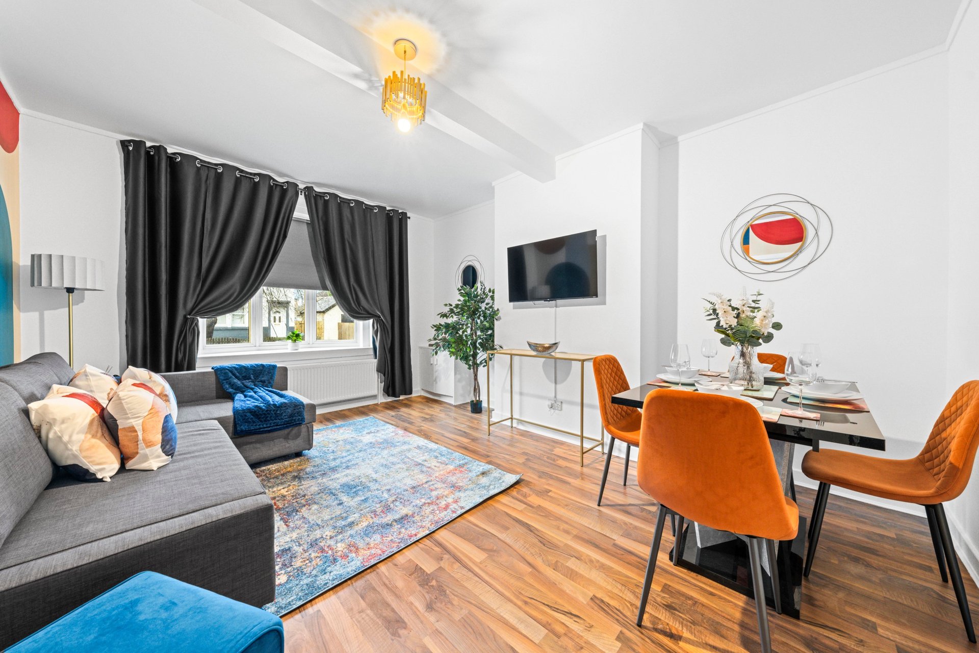 Open-plan living room with gray sofa, dining table, orange chairs, and wooden flooring