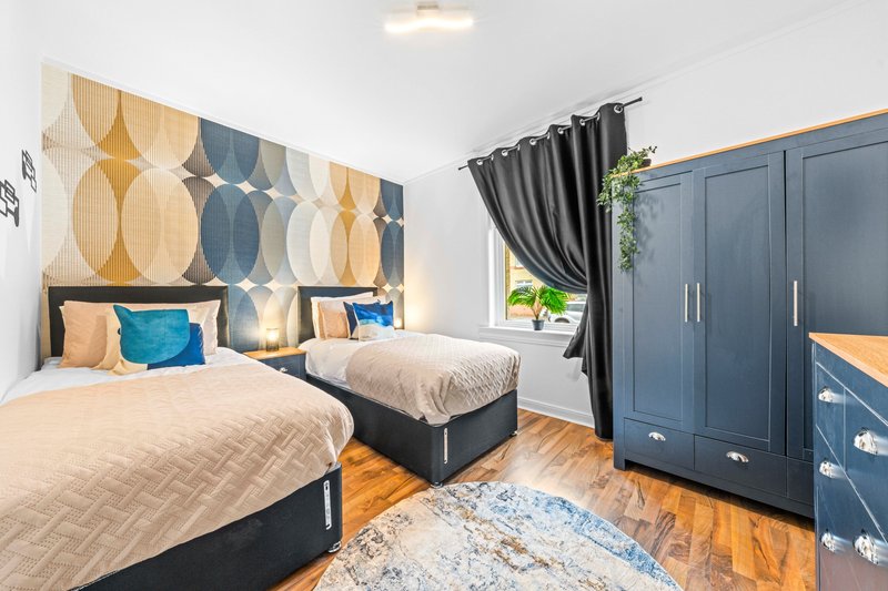 Modern twin bedroom with geometric headboard, navy wardrobes, wooden floor and natural light