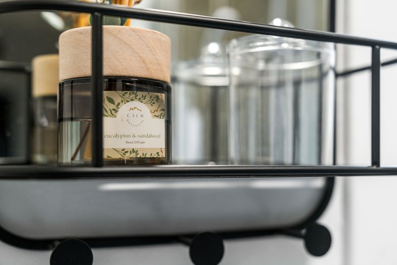Black metal bathroom shelf with eucalyptus candle, glass containers and toiletries