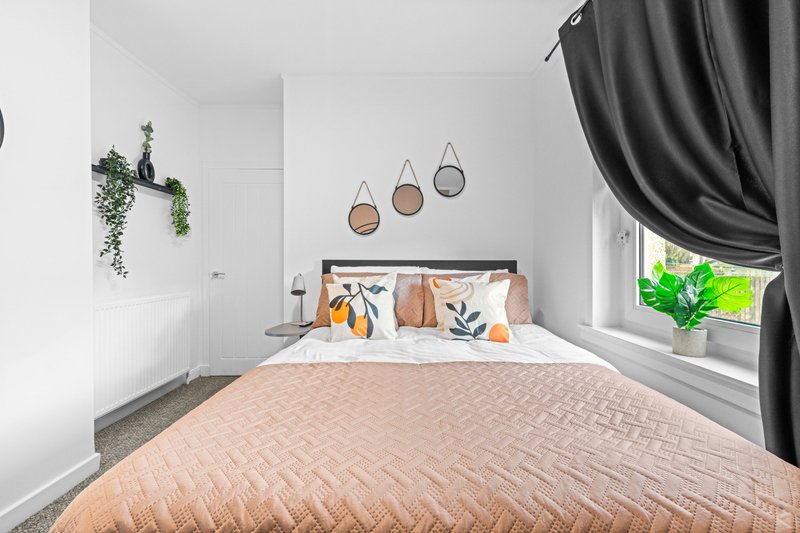 Bright modern bedroom with double bed, decorative wall mirrors, hanging plant, and black curtains