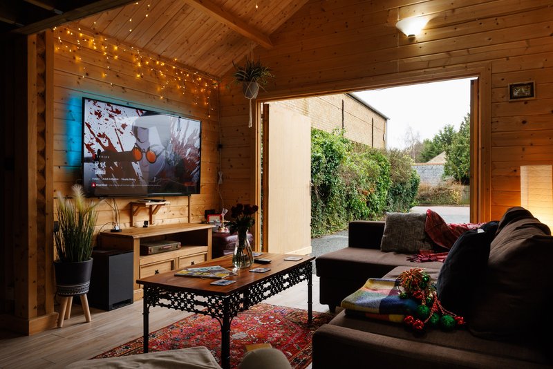 Wooden cabin interior with TV, sofa, coffee table and open patio doors to garden