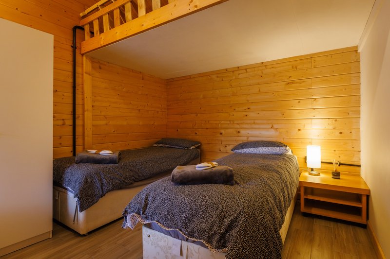 Twin bedroom in wooden cabin with two beds, bedside lamps and natural wood walls