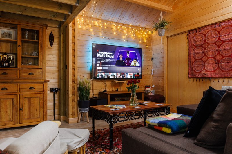 Wooden cabin interior with TV, seating area, decorative lights, and furnished living space