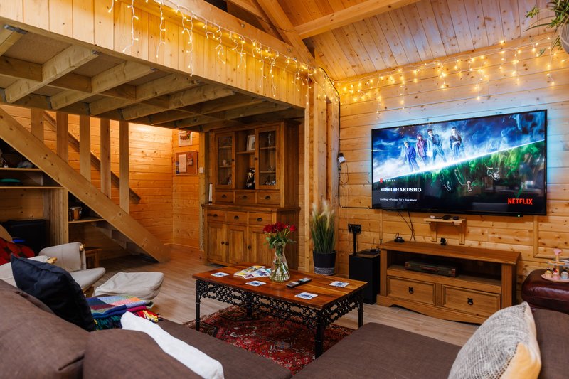 Wooden cabin interior with TV, staircase, seating area and string lights overhead