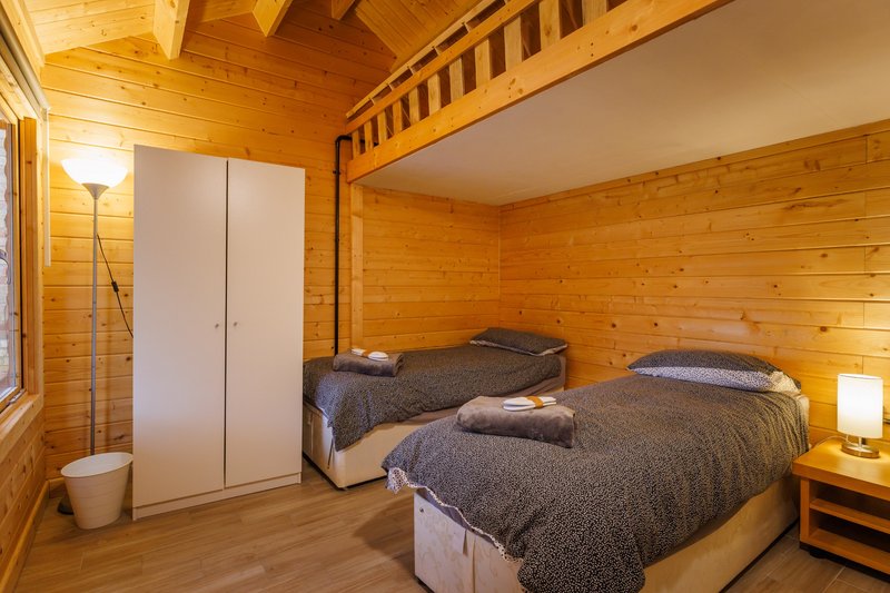 Wooden cabin bedroom with two single beds, bedside lamps, wardrobe and mezzanine area
