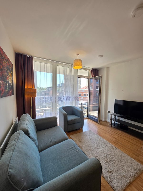 Modern living room with grey upholstered sofa, armchair, TV, wooden flooring and large windows with city views