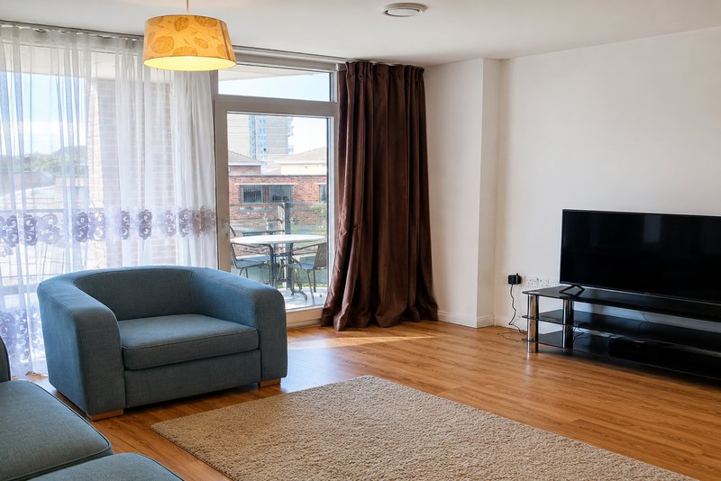 Modern living room with blue armchair, wooden floor, TV unit and city views