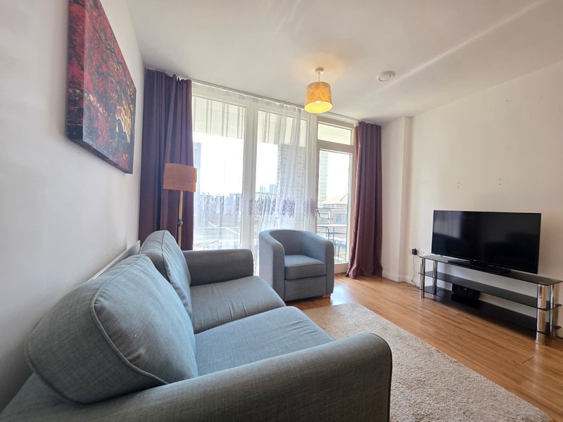 Modern living room with grey sofa, armchair, TV, wooden floor and large windows
