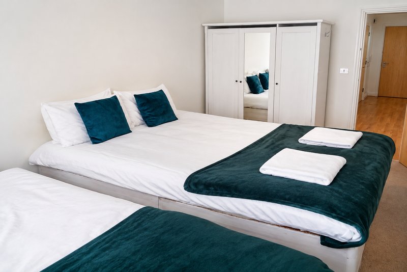 Modern bedroom with two beds, white pillows, dark teal cushions and throws, wooden floor