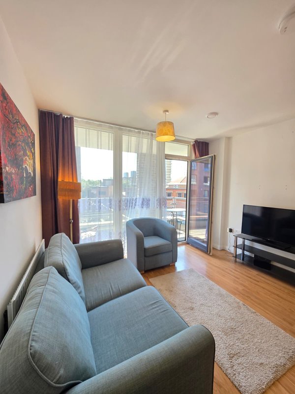 Modern living room with gray upholstered sofa, armchair, wooden floor, and large windows with city views