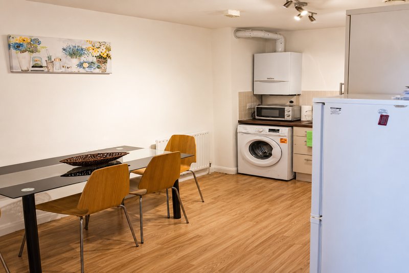Modern kitchen and dining area with wooden table, chairs, washing machine, and appliances