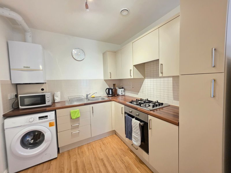 Compact kitchen with cream cabinetry, wooden countertops, washing machine and gas cooker