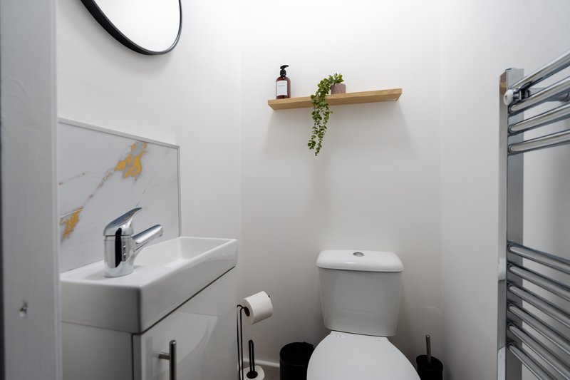 Clean modern bathroom with white toilet, sink, mirror, towel rail and wooden shelf