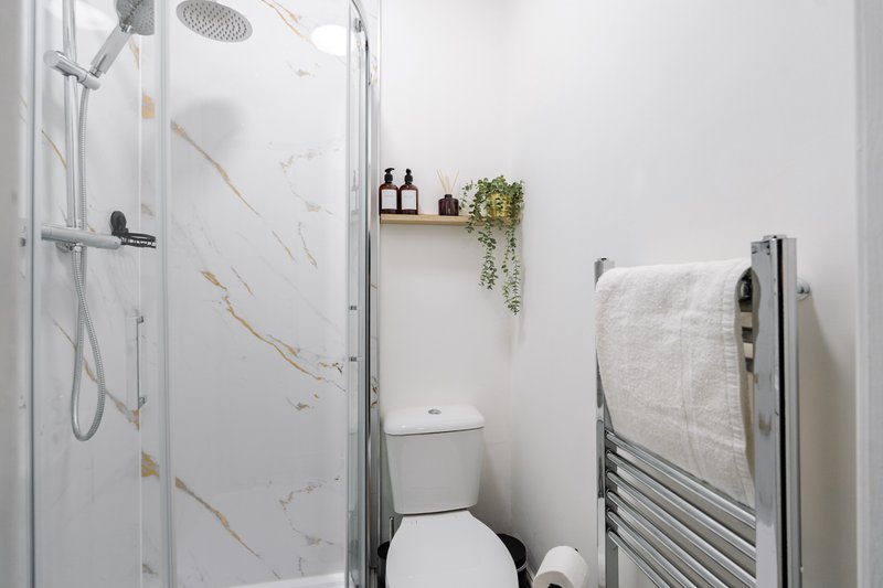 Clean modern bathroom with walk-in shower, toilet, heated towel rail and white wall tiles