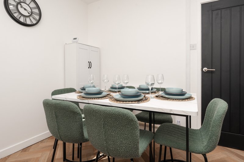 Dining room with set table, green upholstered chairs, wall clock and dark door