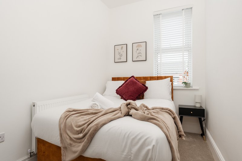 Bright bedroom with wooden bed frame, white bedding, burgundy cushion, and small side table