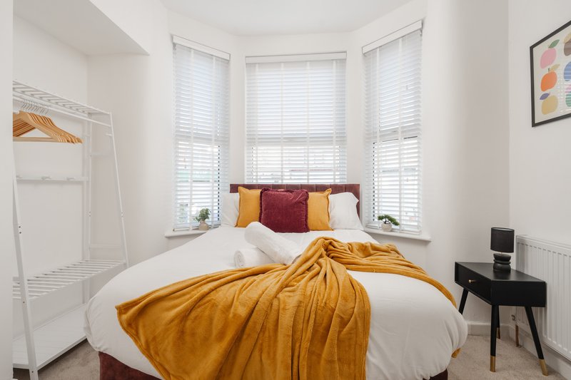 Bright bedroom with double bed, gold throw, colorful pillows and bay window