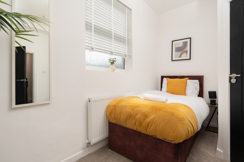 Bedroom with single bed, yellow duvet, white pillows, window with blinds, wall art