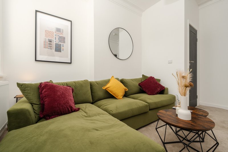 Modern living room with olive green sectional sofa, colorful cushions, round mirror and wooden coffee table