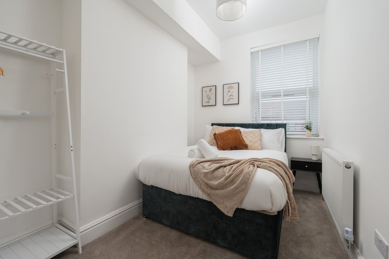 Compact bedroom with single bed, white walls, window with blinds, and ensuite shower room