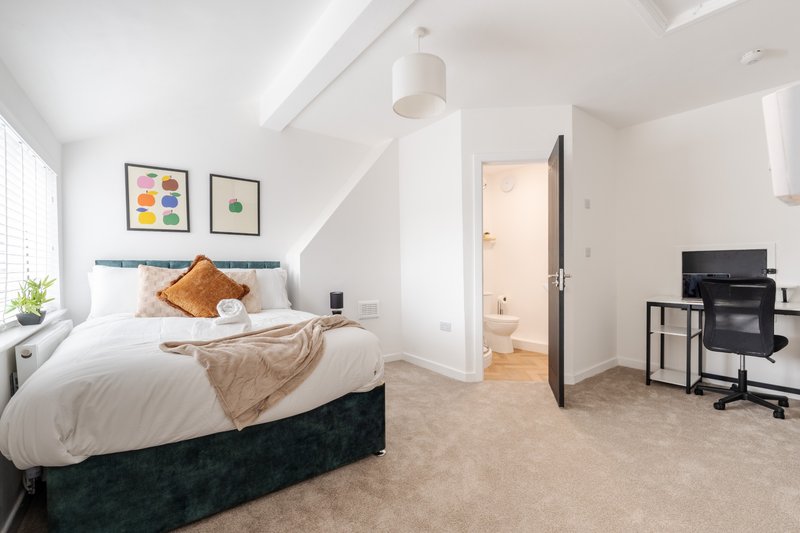 Modern bedroom with double bed, desk area, framed artwork, and ensuite bathroom visible