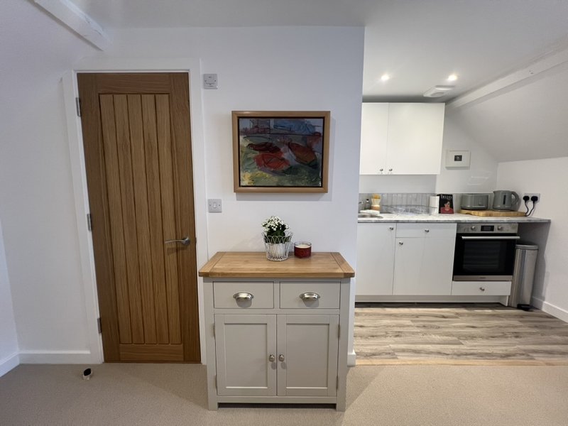 Open-plan kitchen and living area with cream cabinetry, wooden worktop island, and wood-panelled door