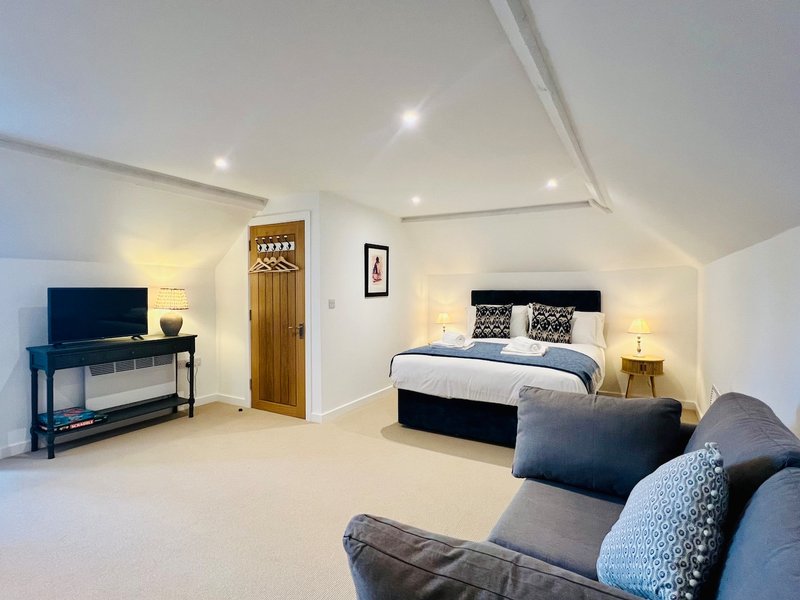 Spacious bedroom with double bed, TV console, armchair and recessed ceiling lights