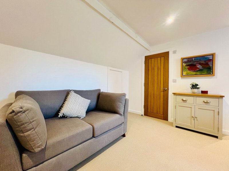 Spacious living room with gray sofa, cushions, wooden door, cream sideboard and framed landscape artwork