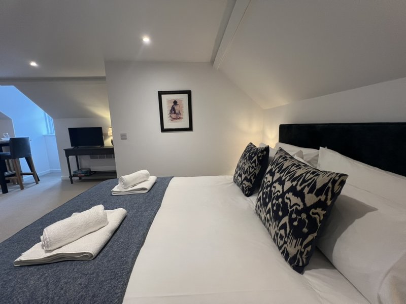 Modern bedroom with double bed, black headboard, patterned cushions, white towels and desk area