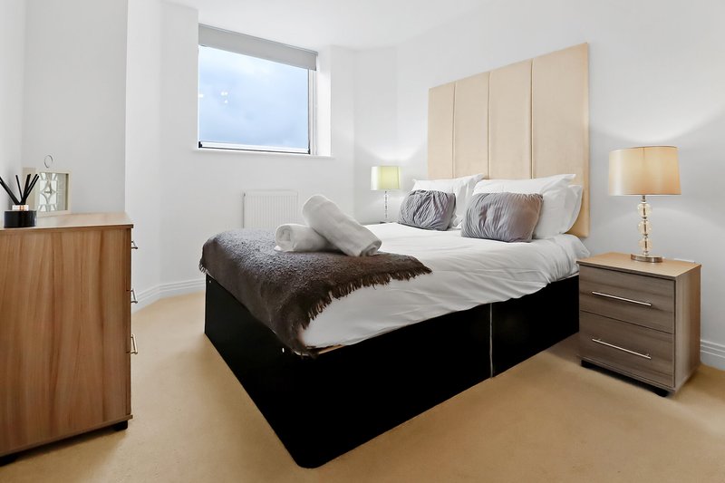 Modern bedroom with double bed, upholstered headboard, bedside table and window