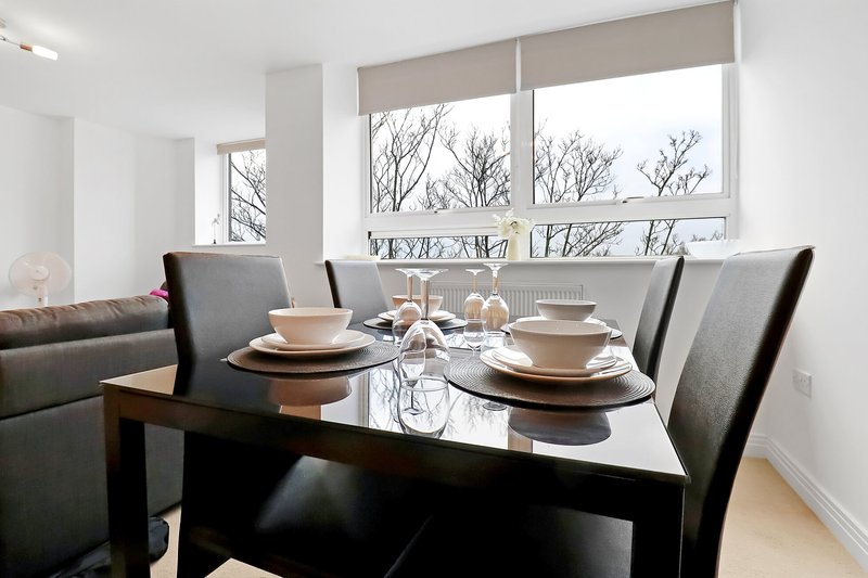 Dining area with black table, grey chairs, place settings, and large windows overlooking bare trees