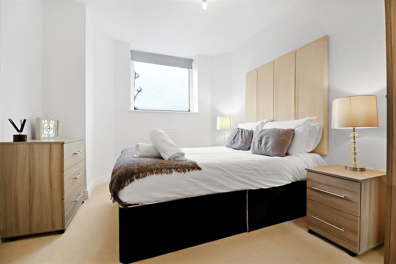 Modern bedroom with double bed, upholstered headboard, wooden furniture and window