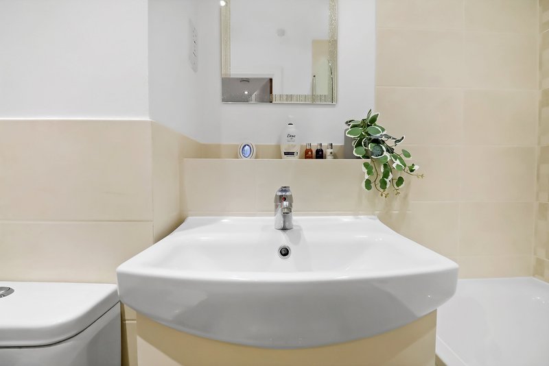 Modern bathroom with curved white sink, mirror, toilet, and potted plant on shelf