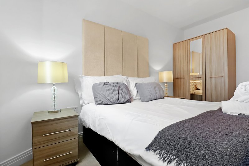 Modern bedroom with double bed, wooden headboard, bedside lamp and wardrobe