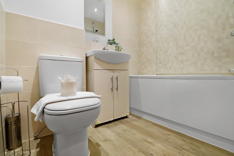 Modern bathroom with toilet, vanity sink, mirror and wooden floor
